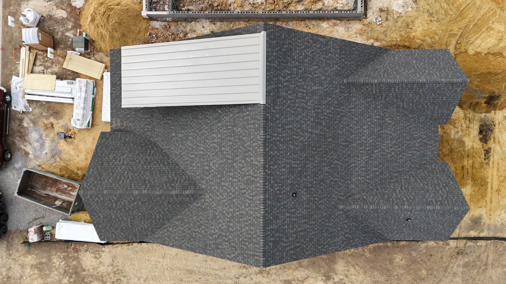 Aerial view of a gray-roofed house under construction on a dirt lot.