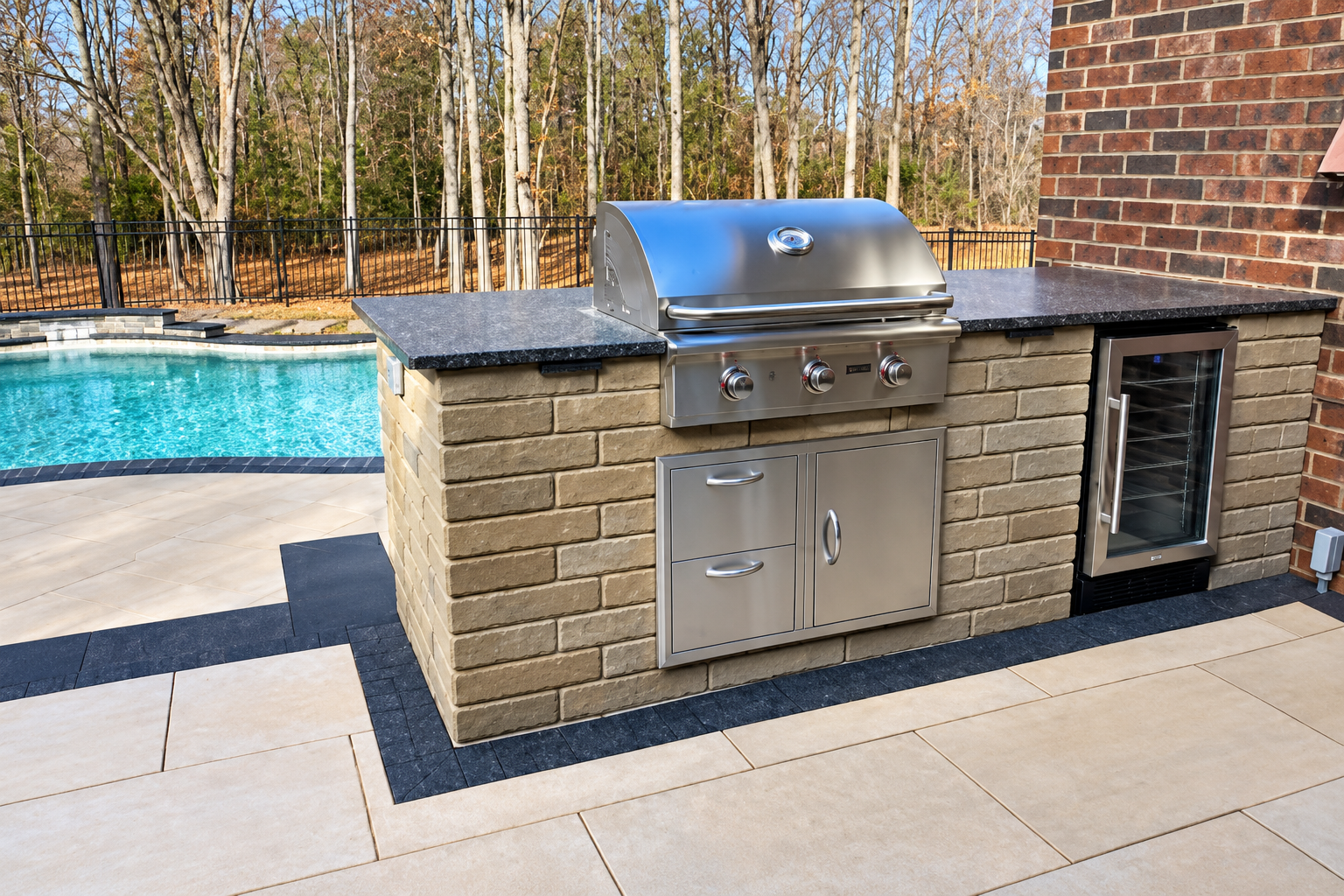Outdoor stainless steel grill and sink setup beside a pool and brick wall on a patio