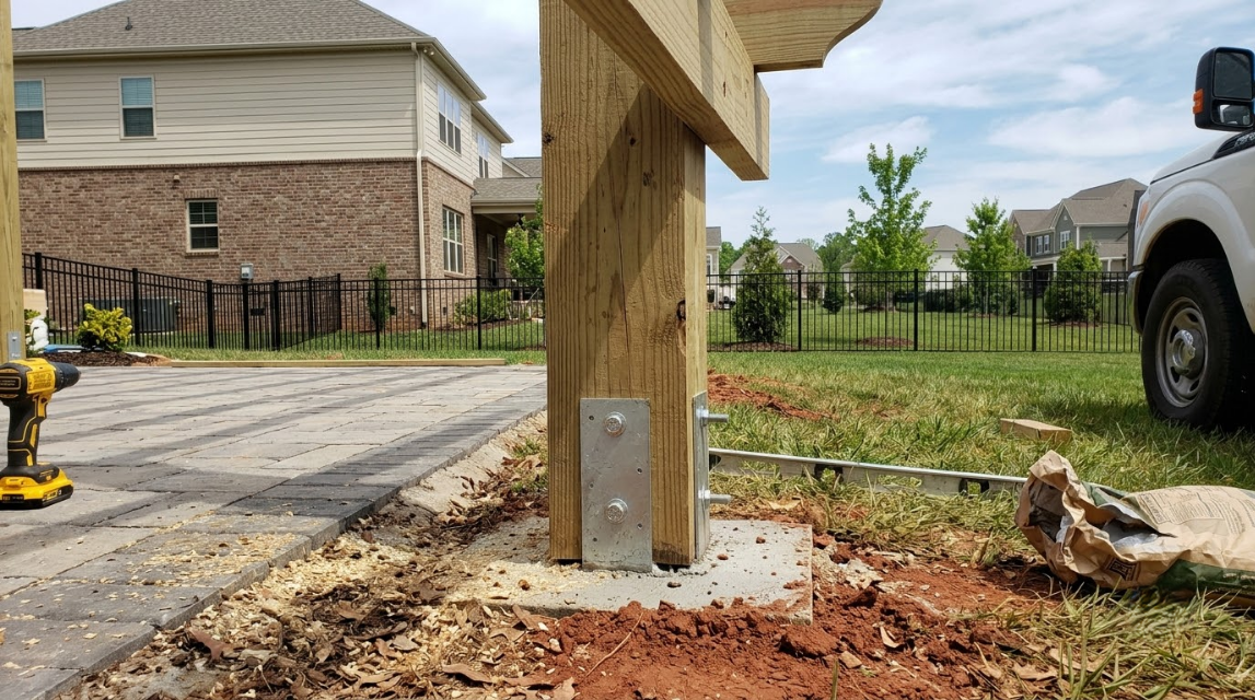 Wooden post anchored in fresh concrete at a residential construction site, with driveway and truck nearby