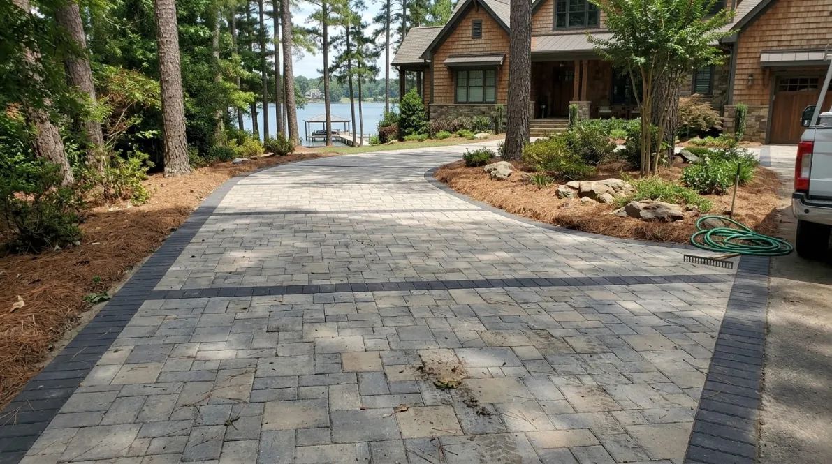 Stone driveway leading to a lakeside cabin, with trees and a parked vehicle on the right.