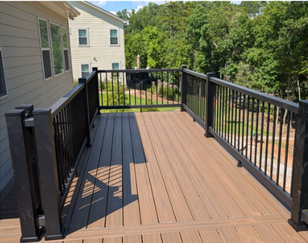 Empty wooden deck with black railing beside a house, overlooking trees and neighboring homes