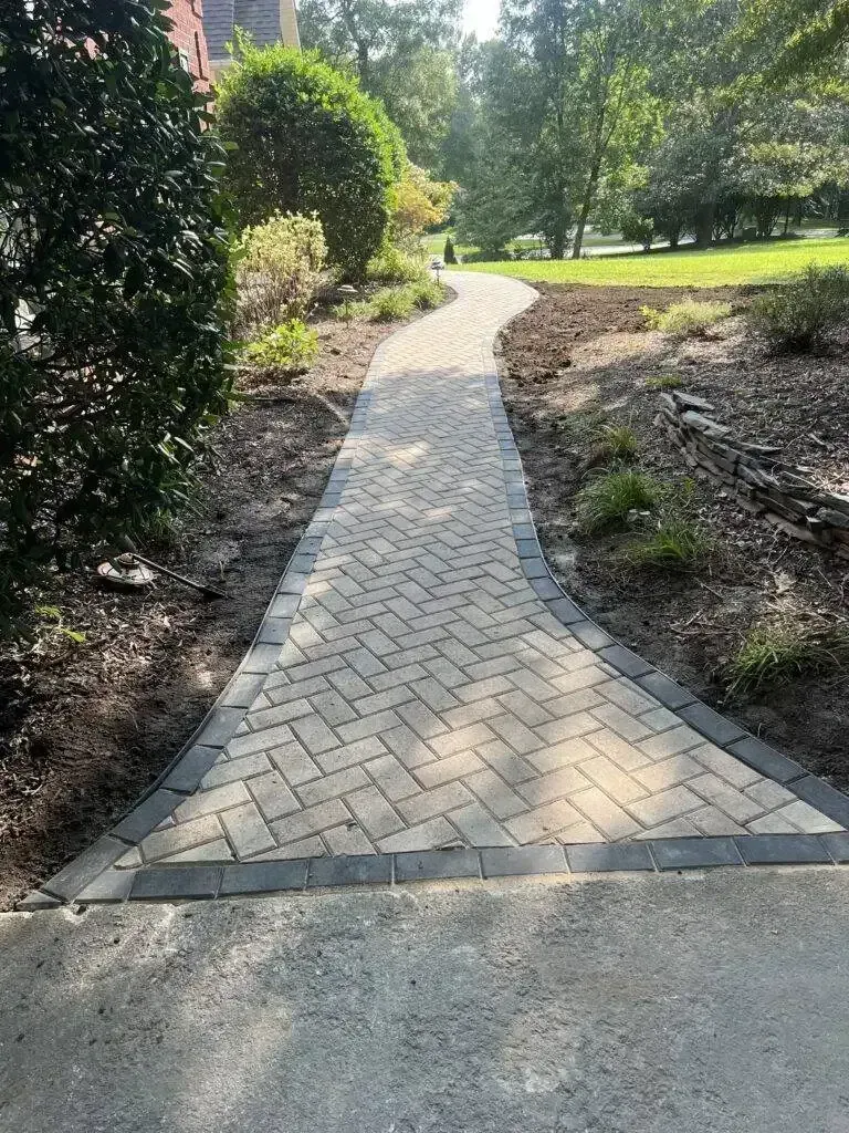 Curved brick walkway through a landscaped park with trees and shrubs in sunlight