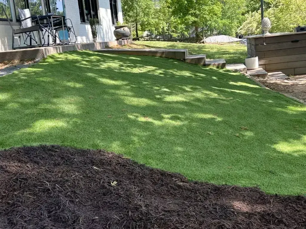 Shaded backyard lawn with a fresh green slope and a dark mulch pile in the foreground.