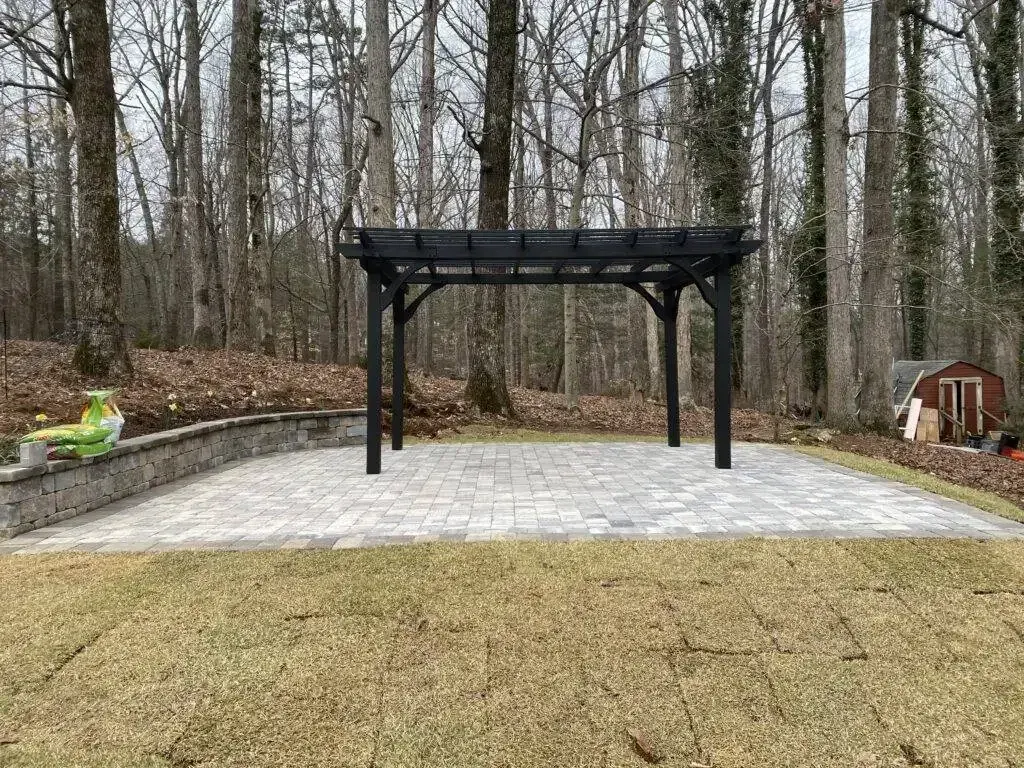 Black pergola on concrete patio in a wooded backyard