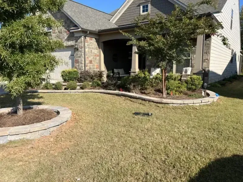 Suburban front yard with curved stone border, lawn, shrubs, and a house entryway