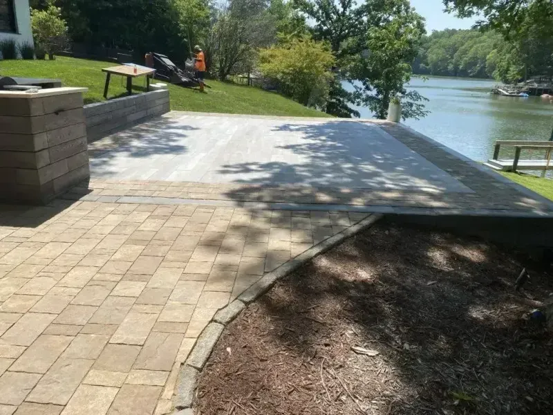 Paved lakeside walkway with brick path, concrete ramp, and shaded trees beside the water