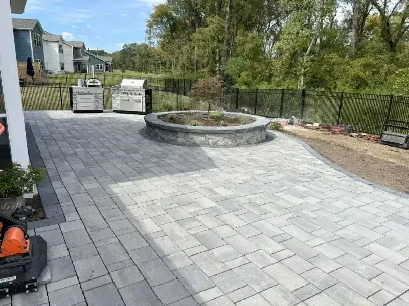 Stone patio with circular planter, gray pavers, and a fenced backyard beside houses