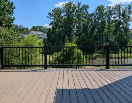 Deck overlooking trees and a house beyond a black metal railing under a clear blue sky