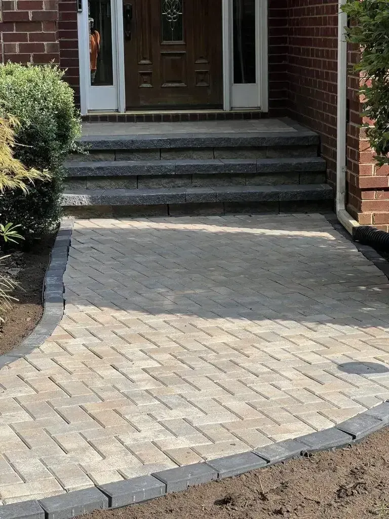 Brick-paved walkway leading to front steps and a dark wooden front door at a house