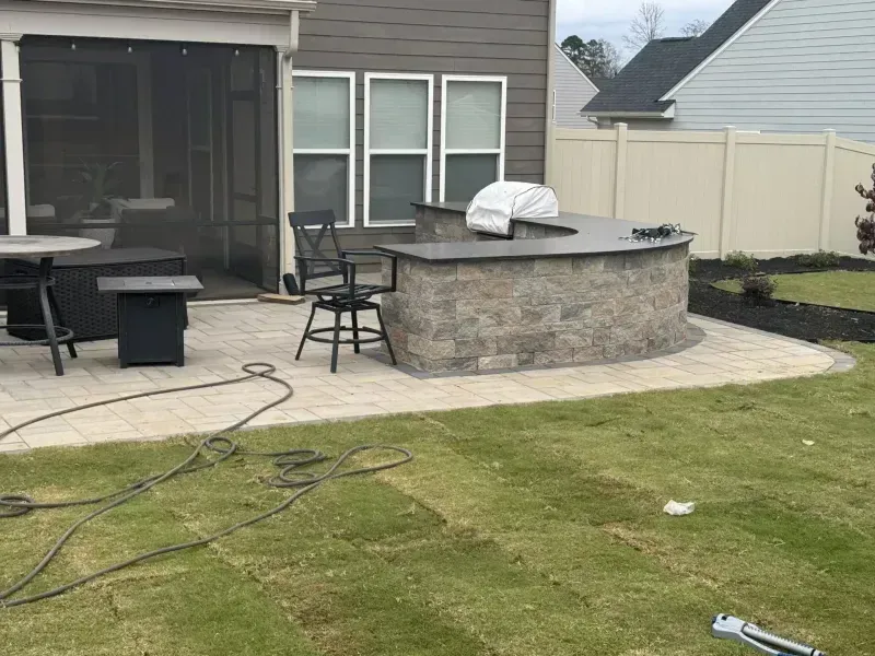 Backyard patio with outdoor furniture, curved stone fire pit, and lawn in front of a screened porch.
