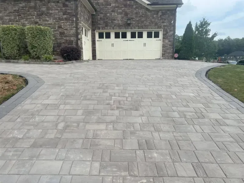 Stone paver driveway leading to a white garage door beside a brick house