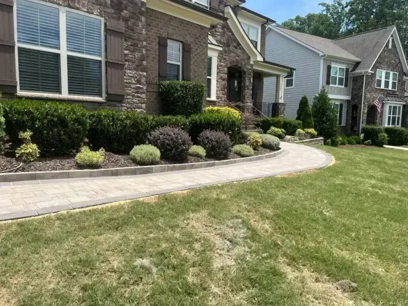 Suburban homes with stone facades, landscaped shrubs, and a curved walkway beside a green lawn