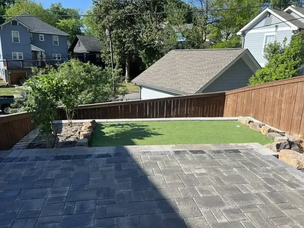Backyard patio with gray pavers, green lawn, stone steps, and wooden fences on both sides