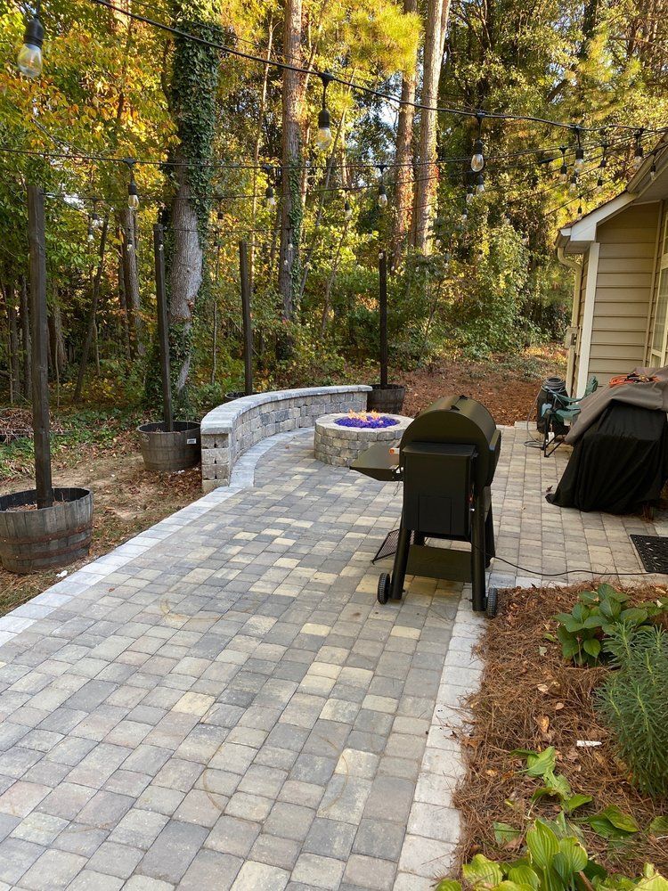 Backyard patio with stone pavers, black chairs, a fire pit, and autumn trees.