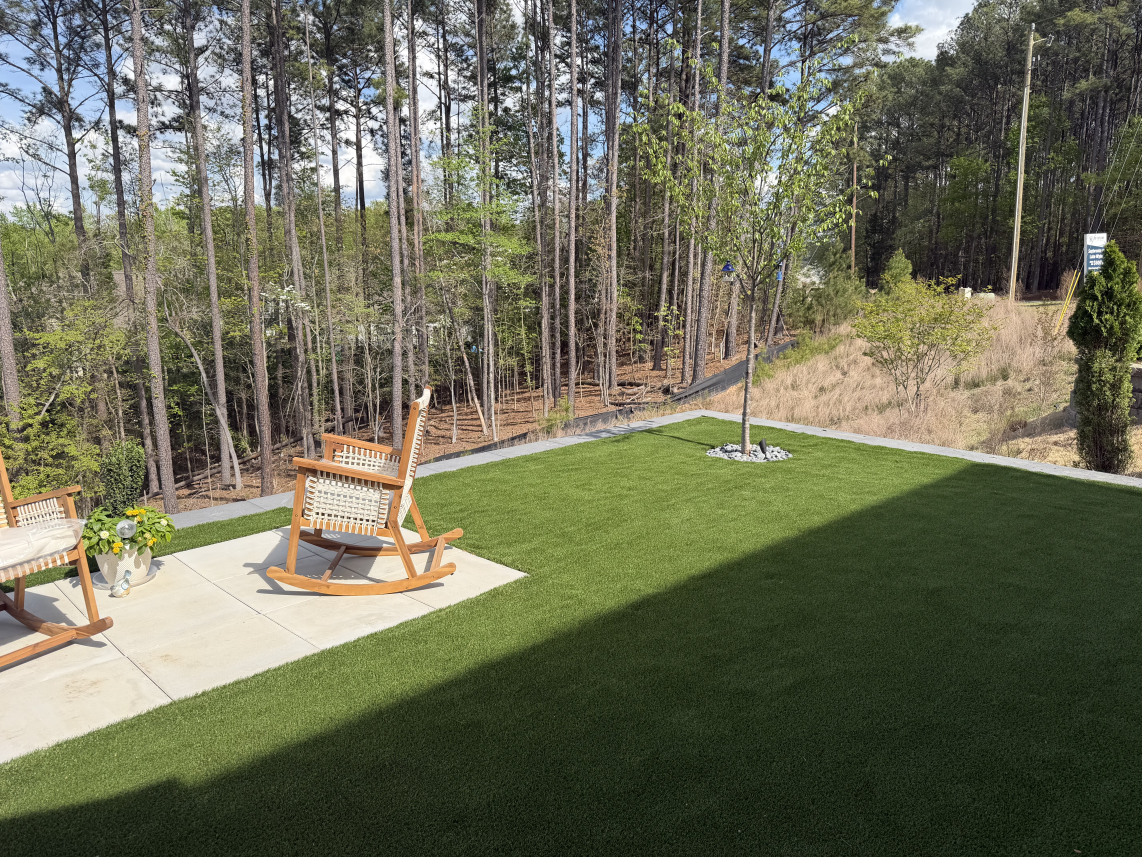 Patio with two wooden rocking chairs beside a green lawn and wooded backyard