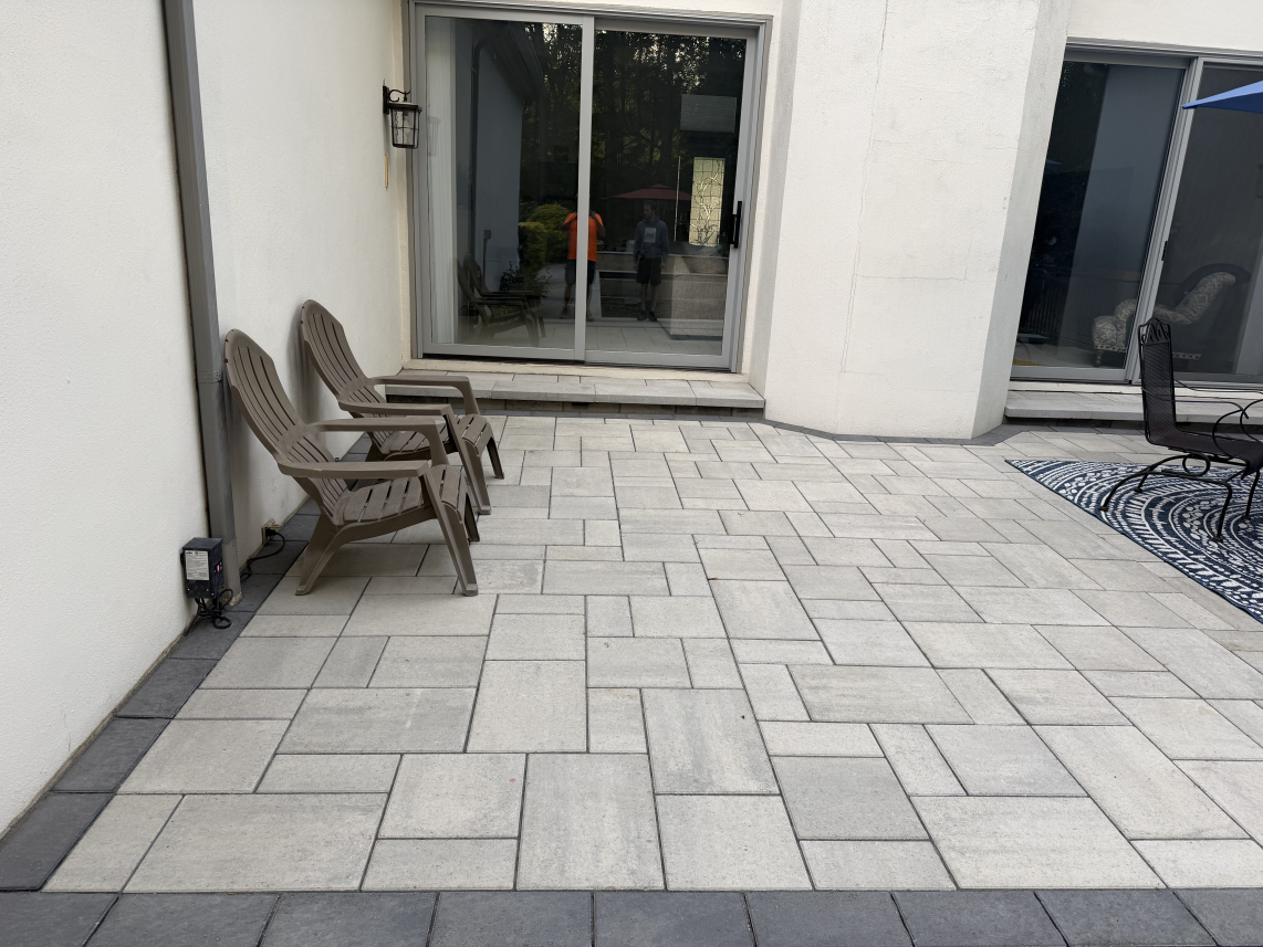 Patio with light gray pavers, two wicker chairs by a sliding glass door, and a gravel bed on the right