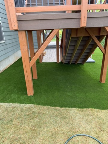 Under-deck area with artificial grass beneath a raised wooden deck and stairs.