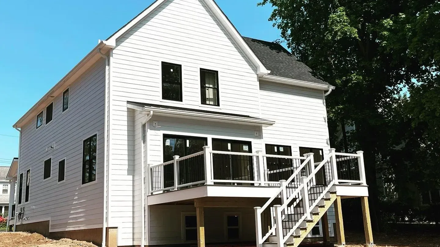 Roofer on a gray shingle roof near a chimney, surrounded by trees and a sunny sky.