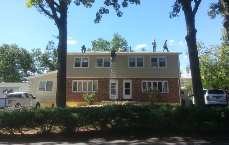 Roof edge with gray shingles and white gutter, overlooking a lawn with a flag.
