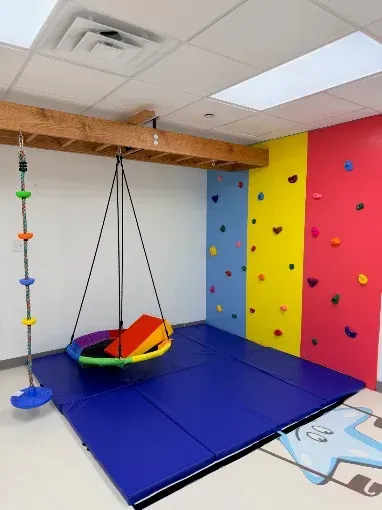 Empty activity room with a colorful climbing wall, swing, and padded floor at Little Stars Pasadena