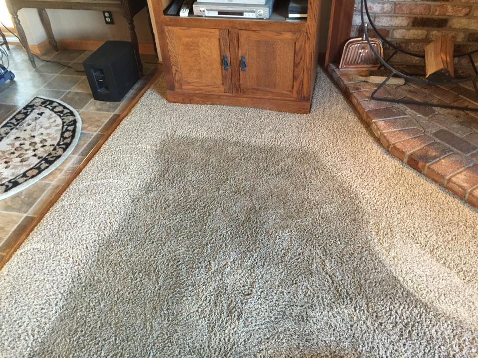 Small beige rug on a carpeted living room floor beside a brick hearth and wooden TV cabinet.
