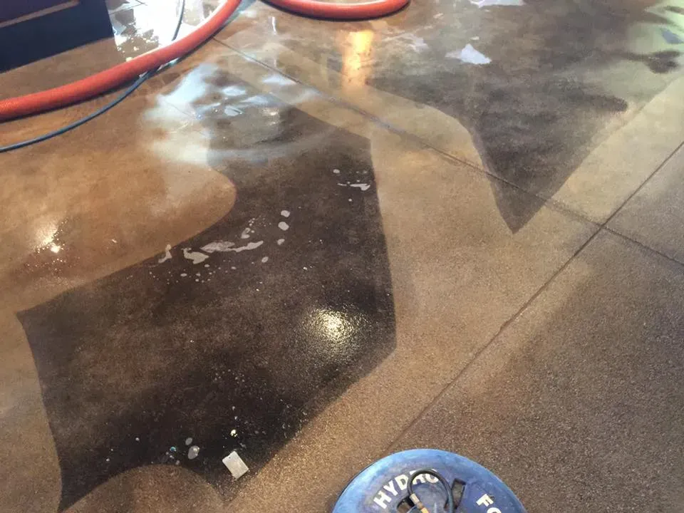 Wet concrete floor with dark patches, red hose, and a blue hydrant cap in the corner