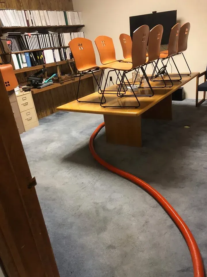 Chairs stacked on a table in a room, with a red hose on the floor and shelves in the background