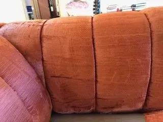 Close-up of an orange-brown upholstered couch with visible seams and a pink cushion on the left