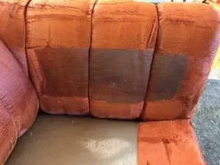 Orange upholstered couch with visible dark stains on the seat and backrest