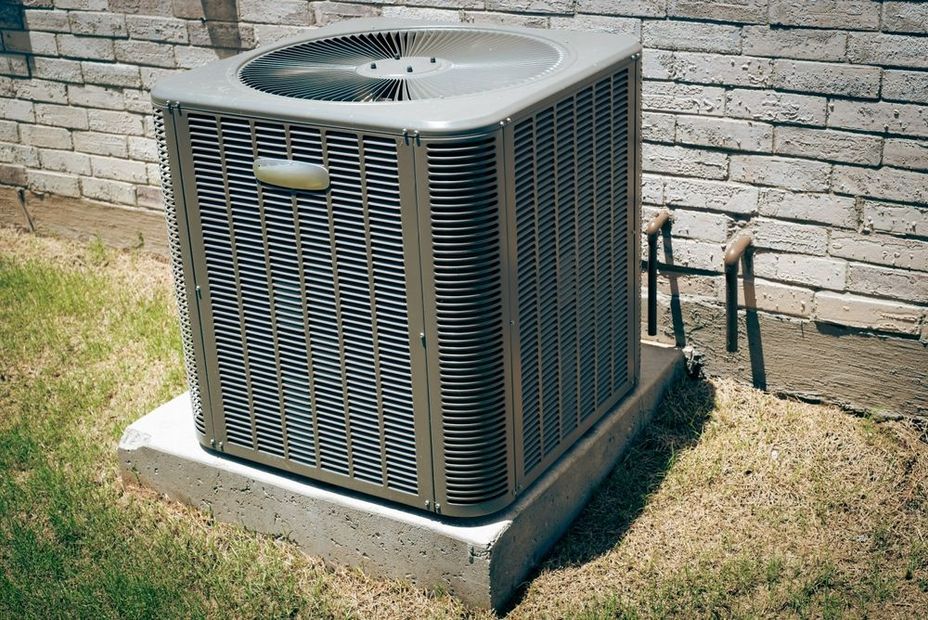 Central air conditioning unit outside on concrete base, next to a brick wall.