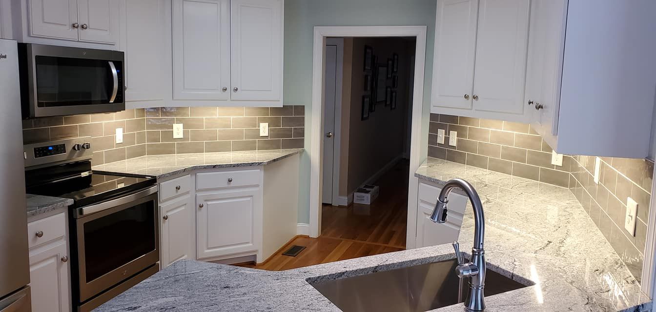 A modern kitchen with white cabinets, speckled granite countertops, a stainless steel oven, and gray subway tile backsplash.