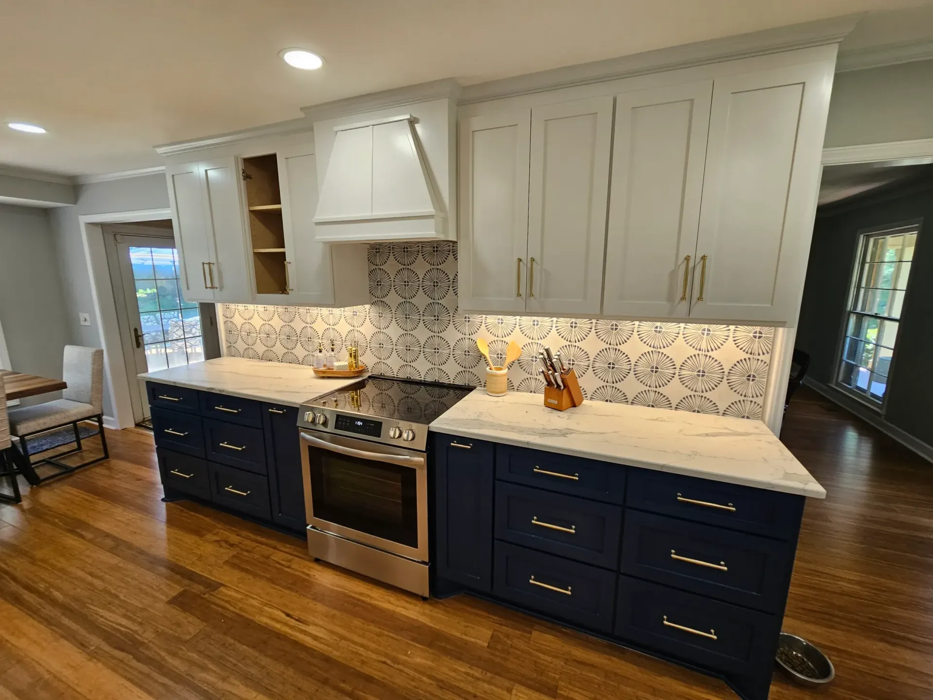 Kitchen with navy lower cabinets, white upper cabinets, gold hardware, marble countertops, and patterned backsplash.