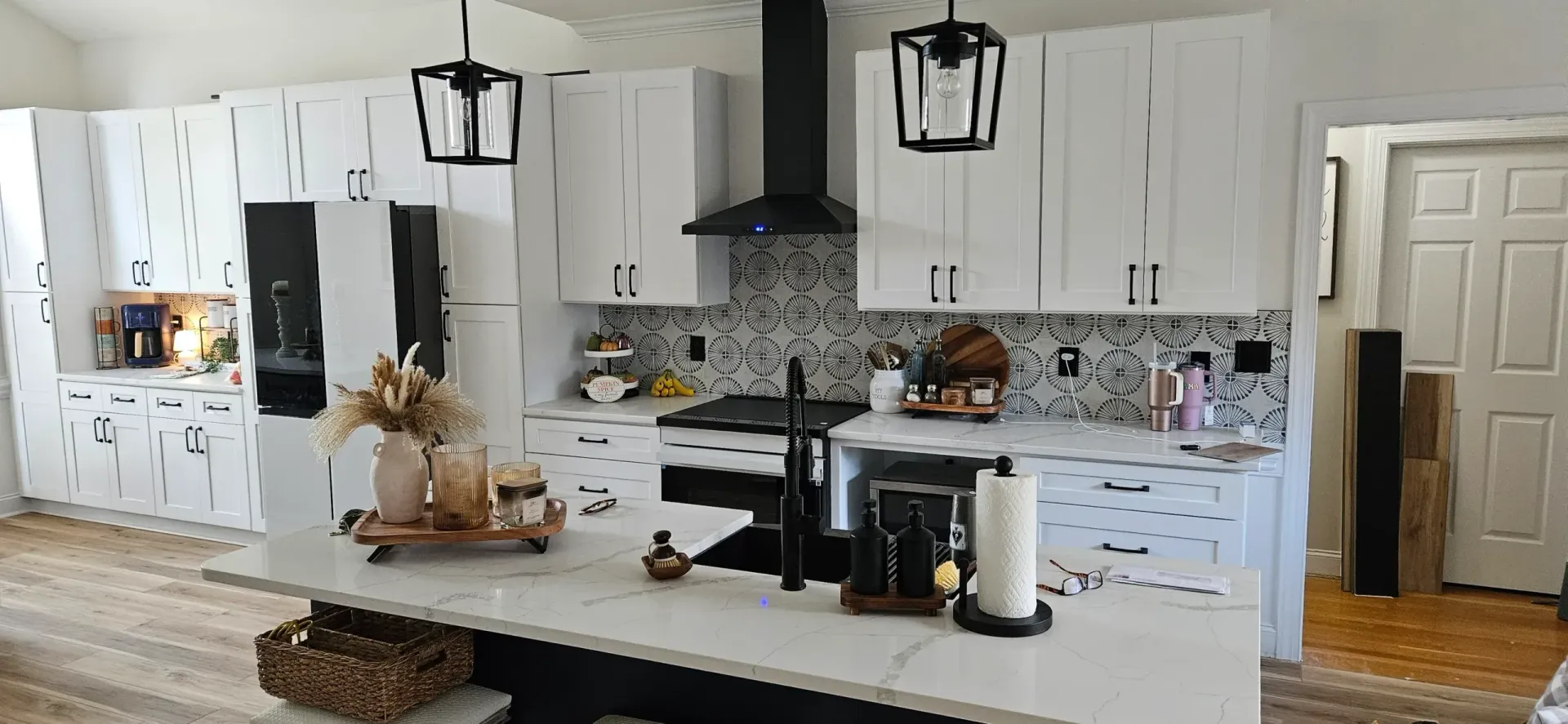 Modern kitchen featuring white cabinets, a black hood, a central island with a white countertop, and patterned backsplash.