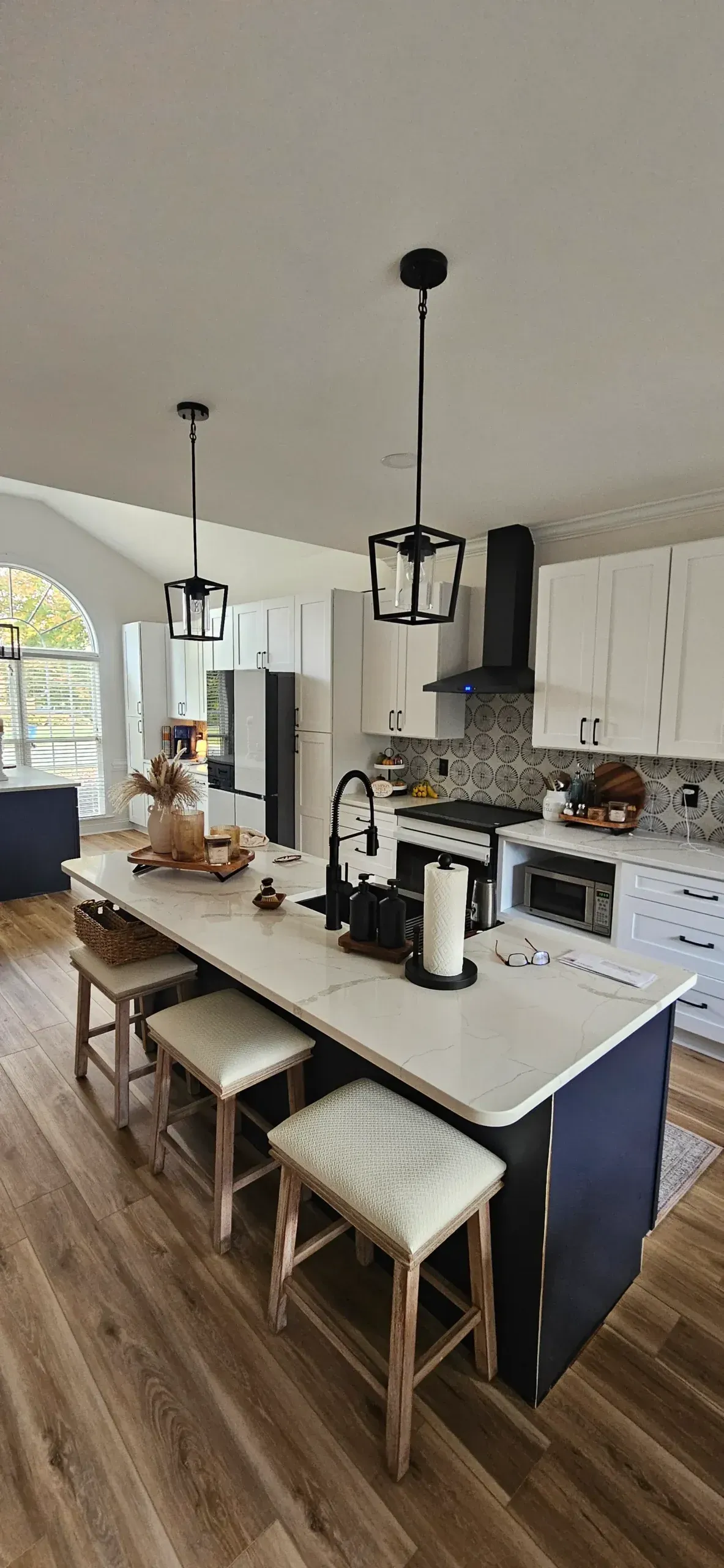 A bright kitchen features a dark blue island with light countertops, three stools, and two pendant lights above.