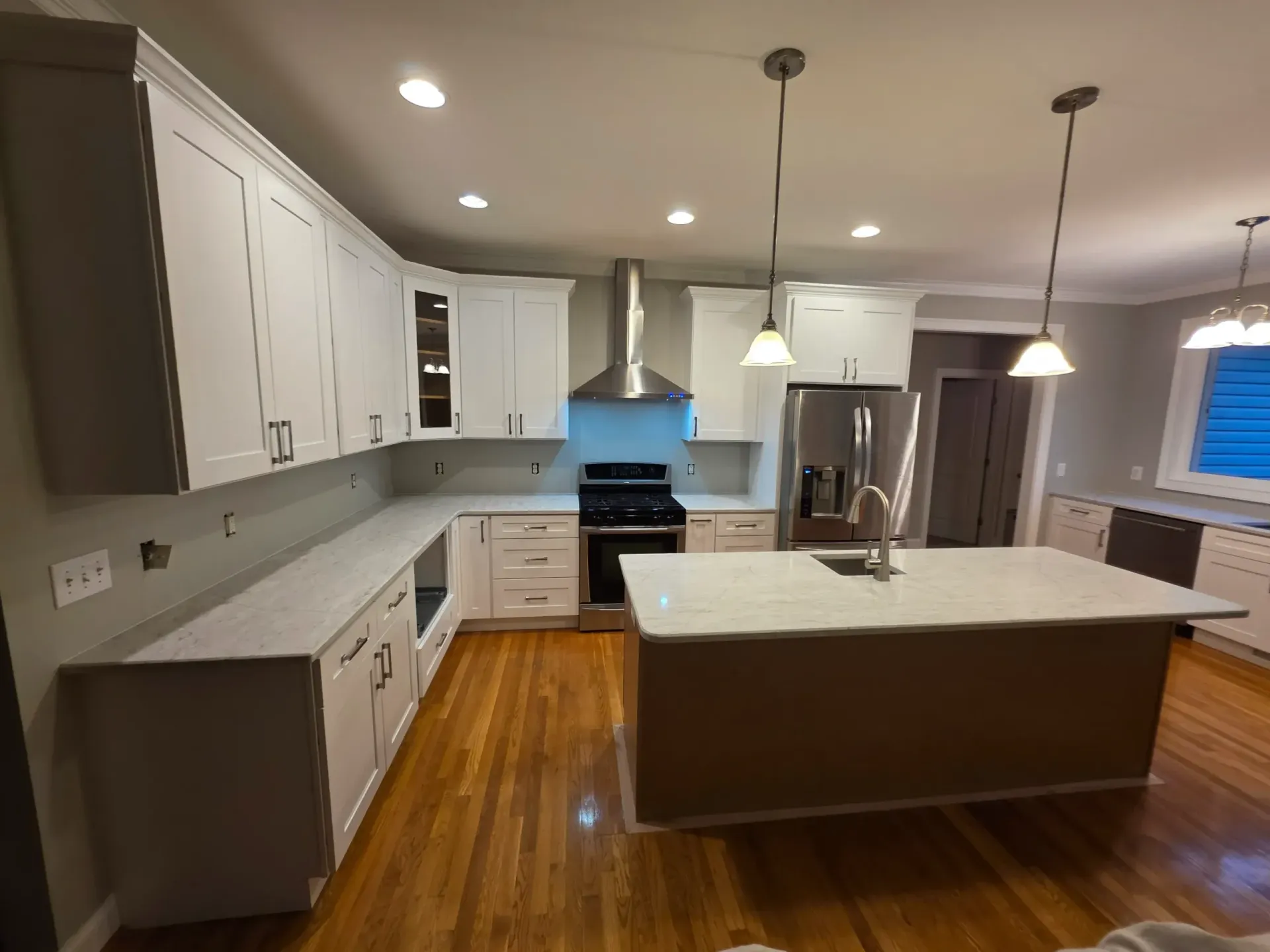 Modern kitchen with white cabinets, light quartz countertops, stainless steel appliances, and a central island on wood floors.