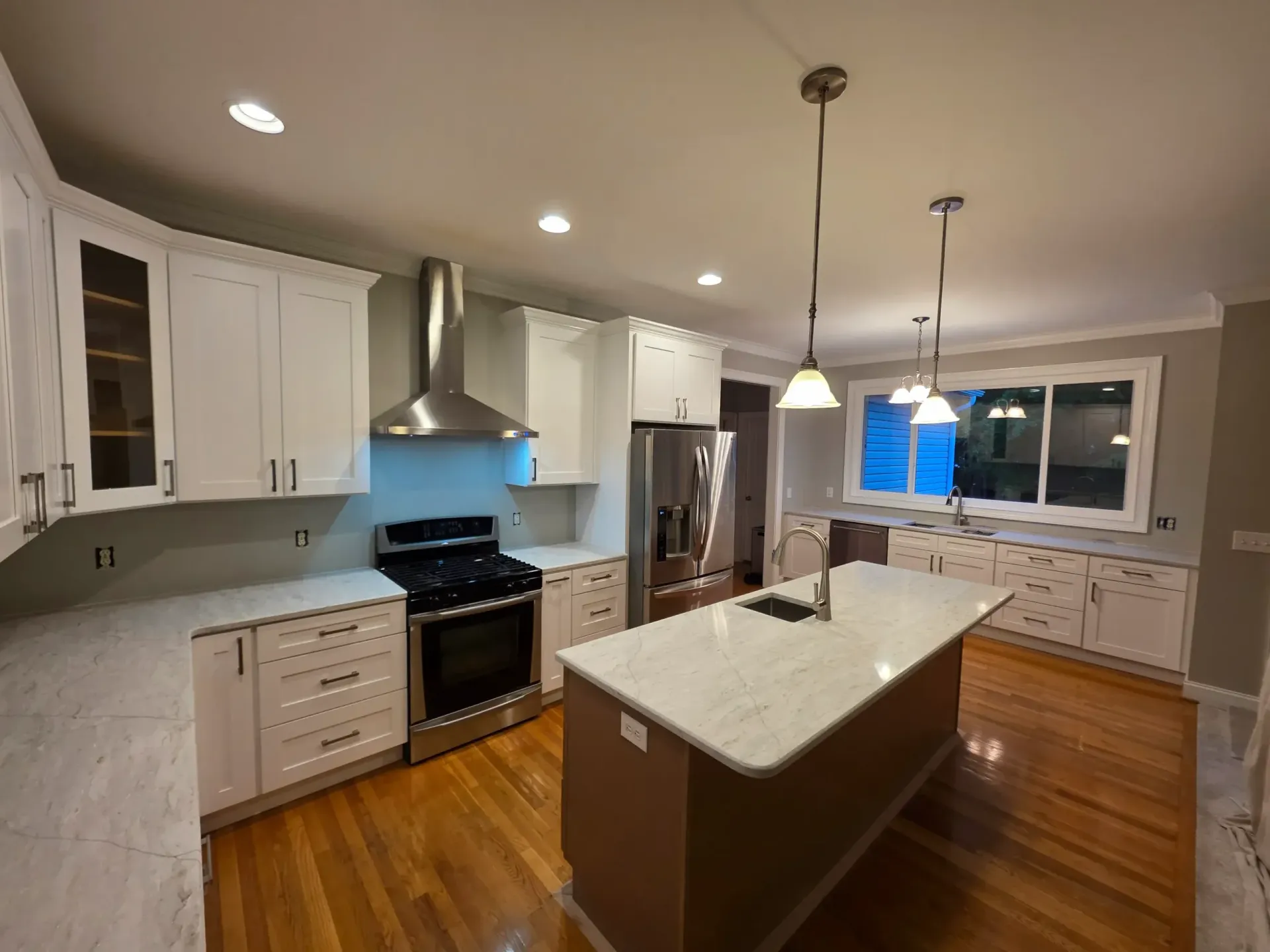A renovated kitchen featuring white cabinets, stainless steel appliances, a marble-topped island, and hardwood floors.