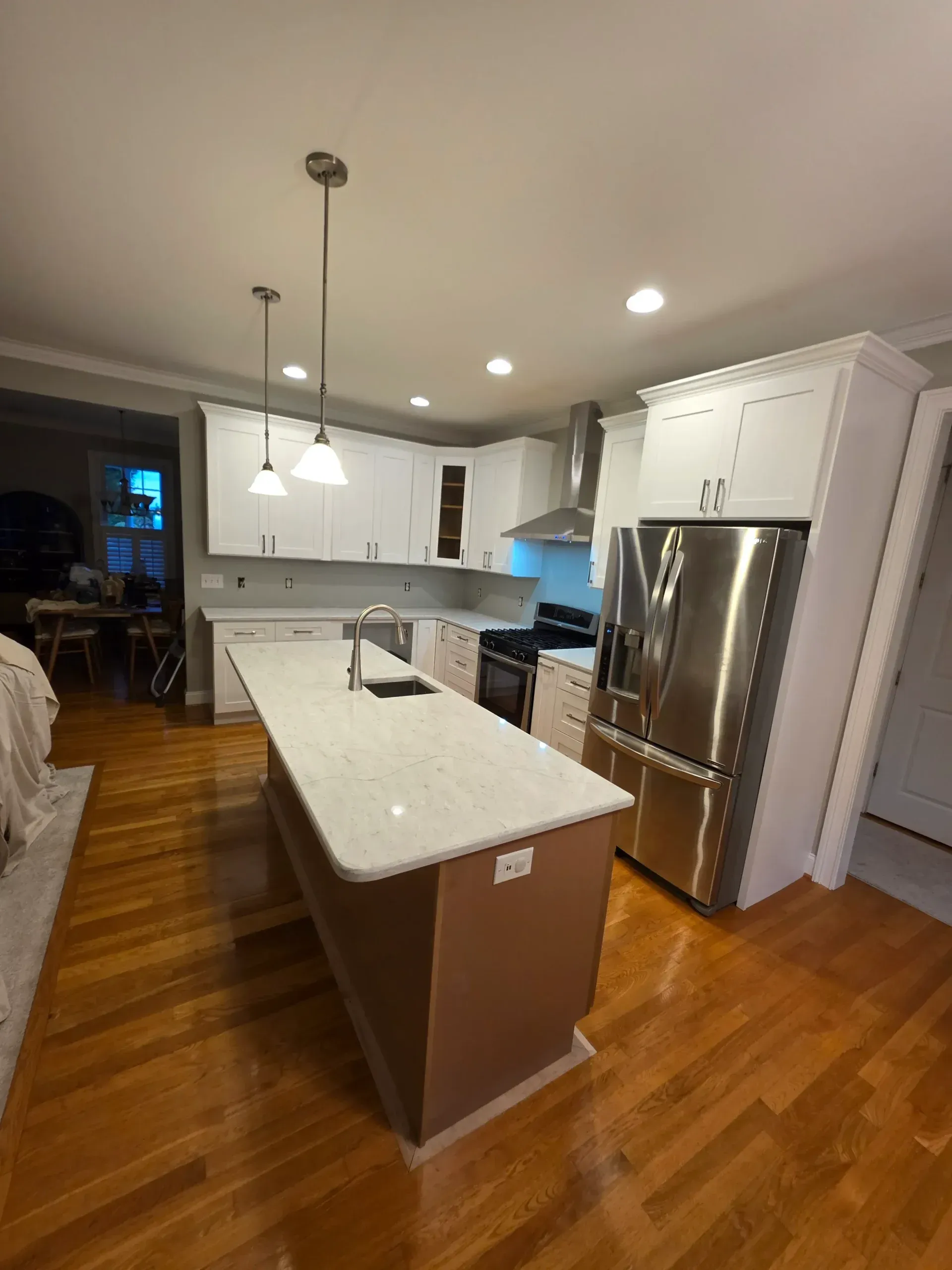 Modern kitchen with a light granite island, white cabinets, stainless steel appliances, and polished hardwood flooring.