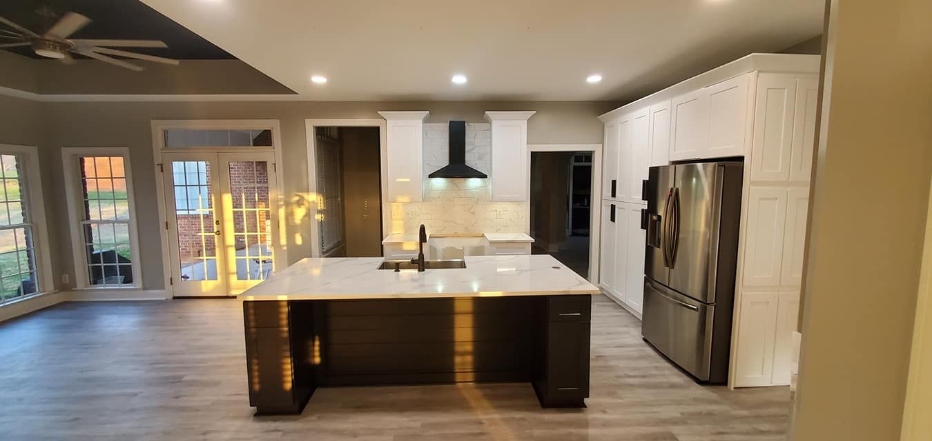 Modern kitchen featuring white cabinets, a dark central island, stainless steel refrigerator, and recessed lighting.