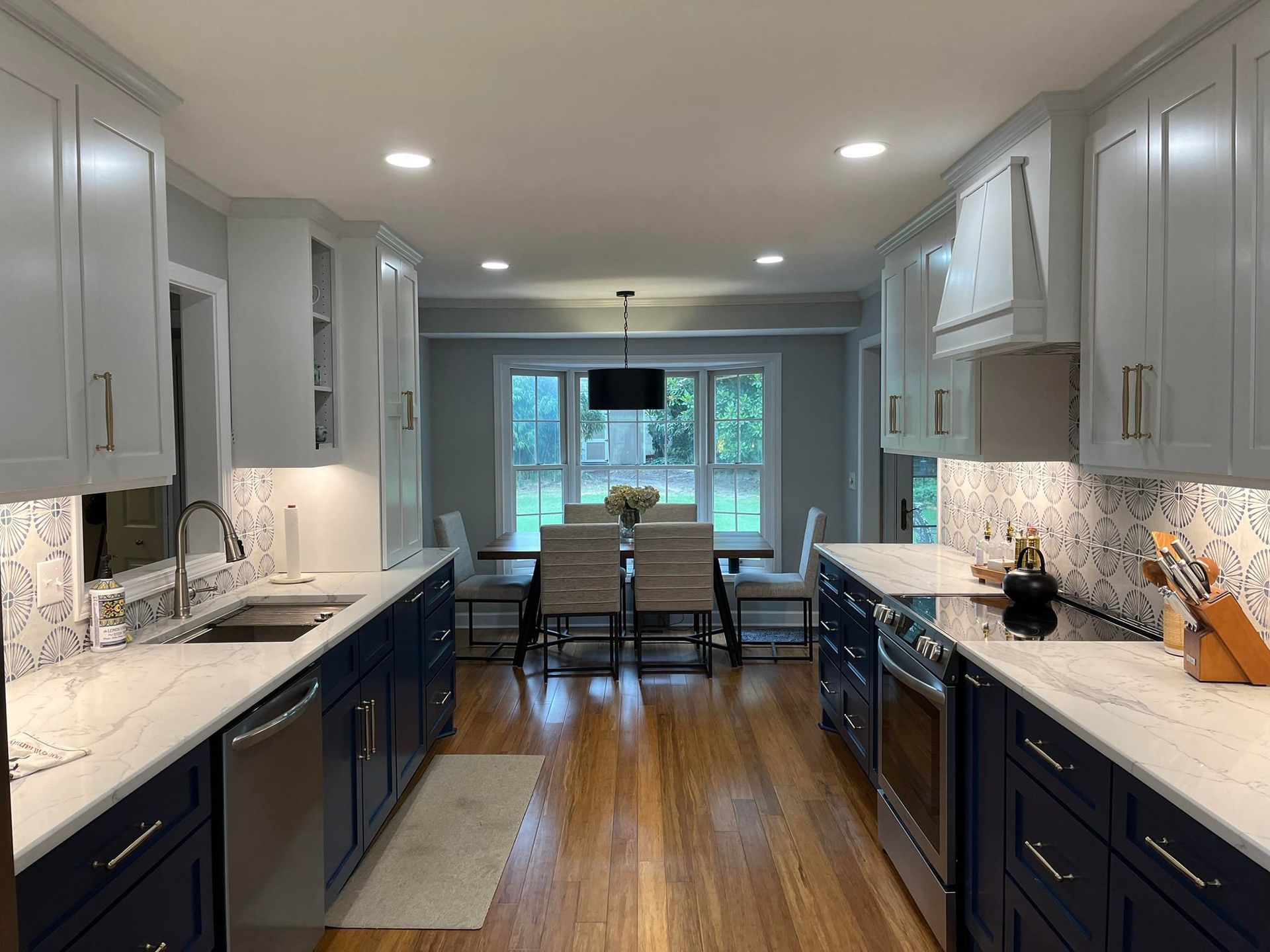 A modern kitchen with navy blue lower cabinets, white upper cabinets, white countertops, and a dining area in the back.