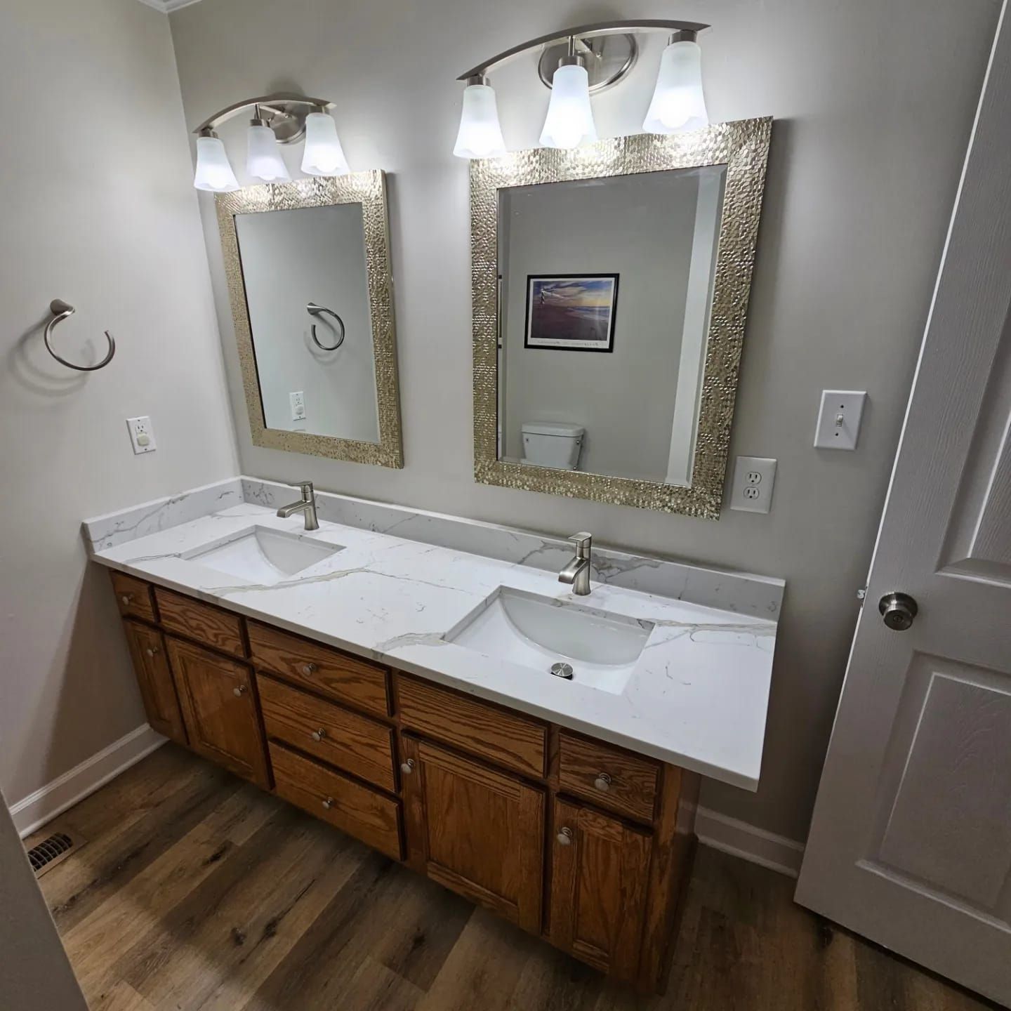 Double bathroom vanity with a white marble-patterned countertop, two sinks, wood cabinets, and two mirrors with lighting.