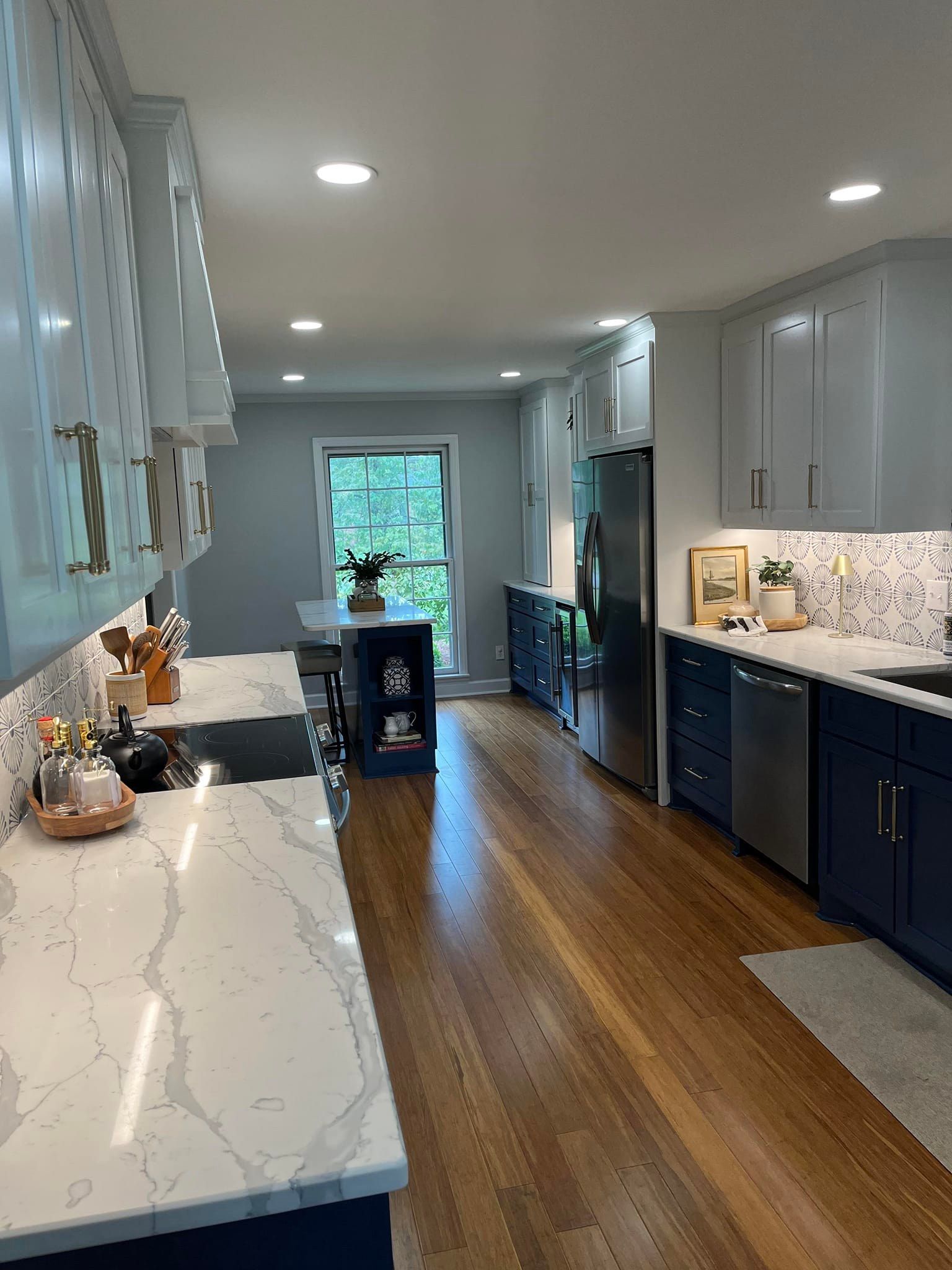 A long, galley-style kitchen with navy cabinets, white marble-look countertops, stainless steel appliances, and wood floors.