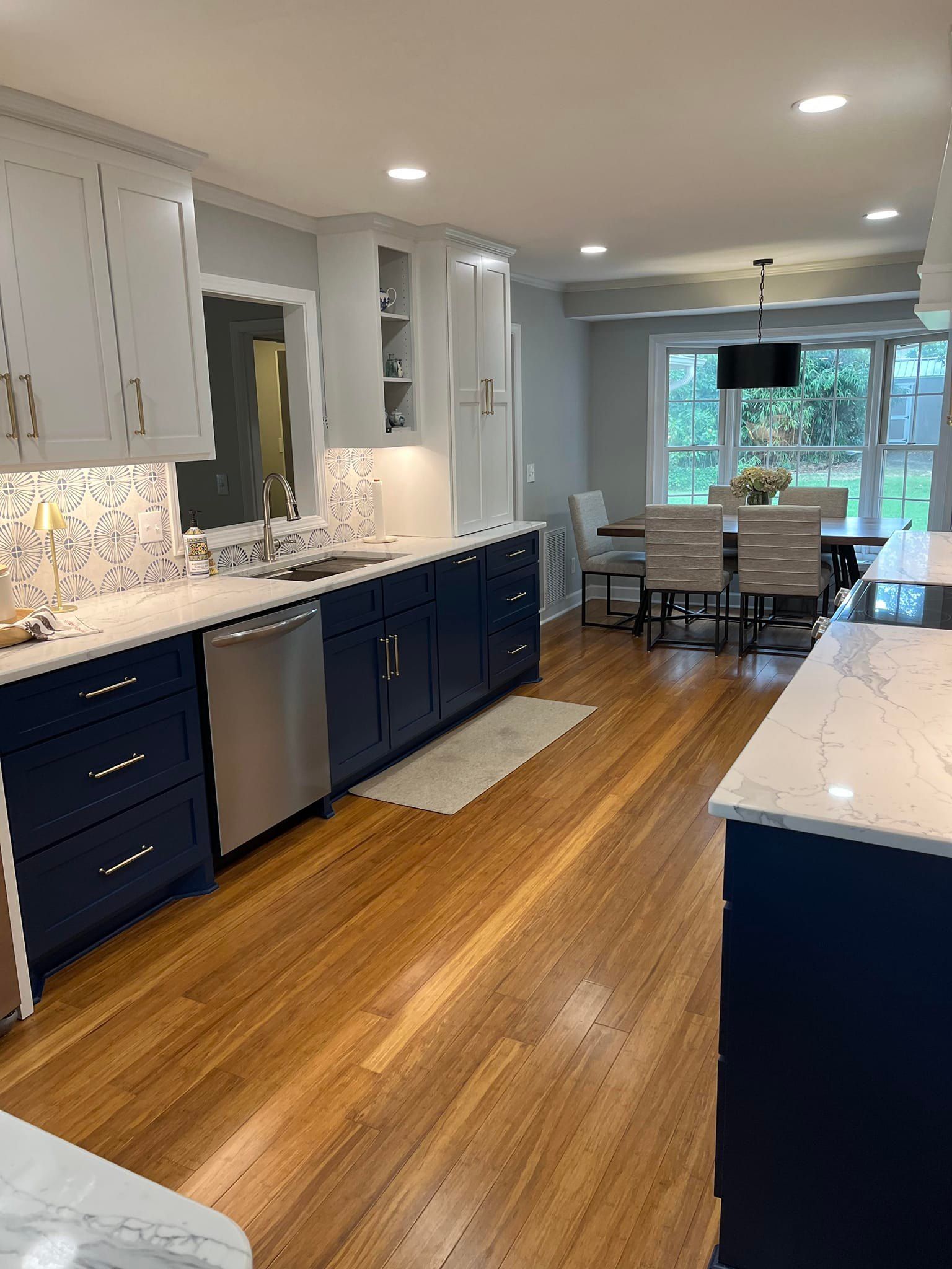 A kitchen with dark blue lower cabinets, white upper cabinets, marble-patterned countertops, and light wood floors.
