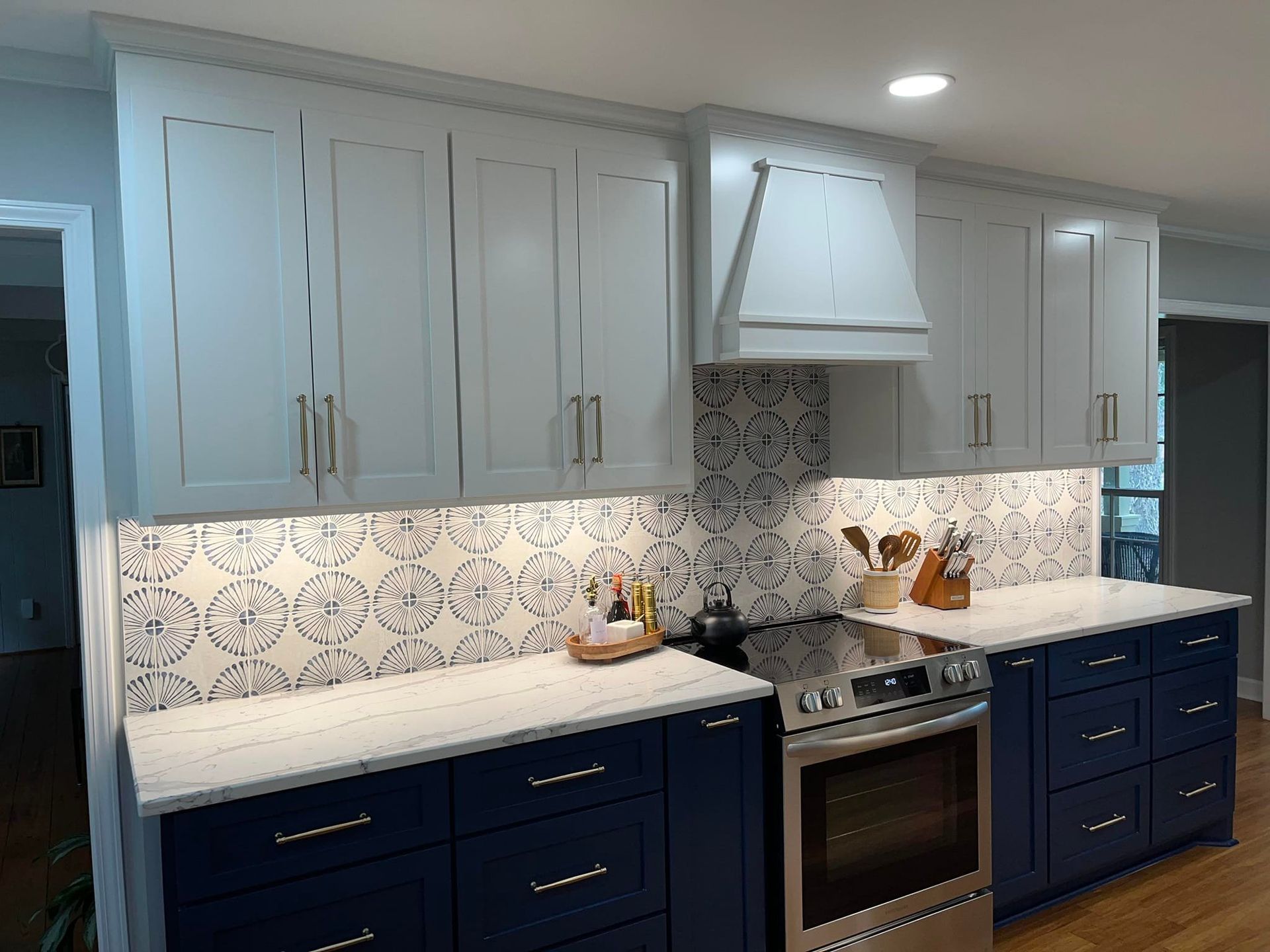 A kitchen with navy blue base cabinets, white upper cabinets, a patterned tile backsplash, and stainless steel stove.