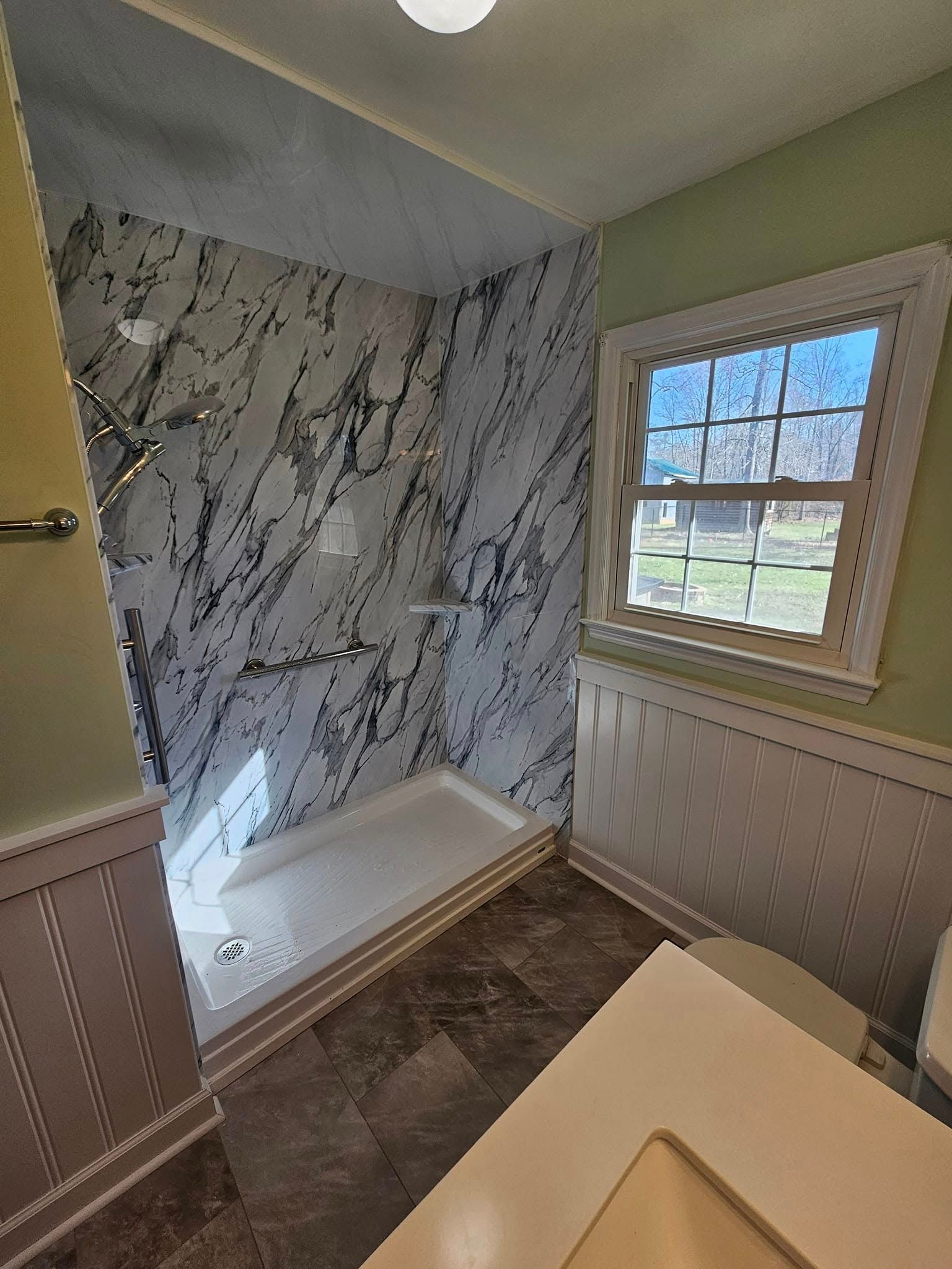 A bathroom featuring a walk-in shower with black-and-white marble-patterned walls, dark tile floors, and a sunny window.