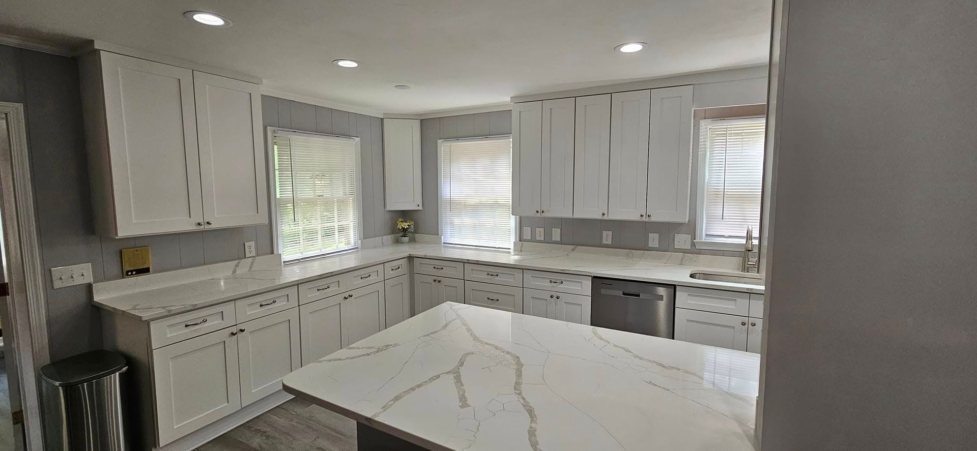 A bright, modern kitchen with white cabinets, a large white marble-patterned island, and light gray walls.