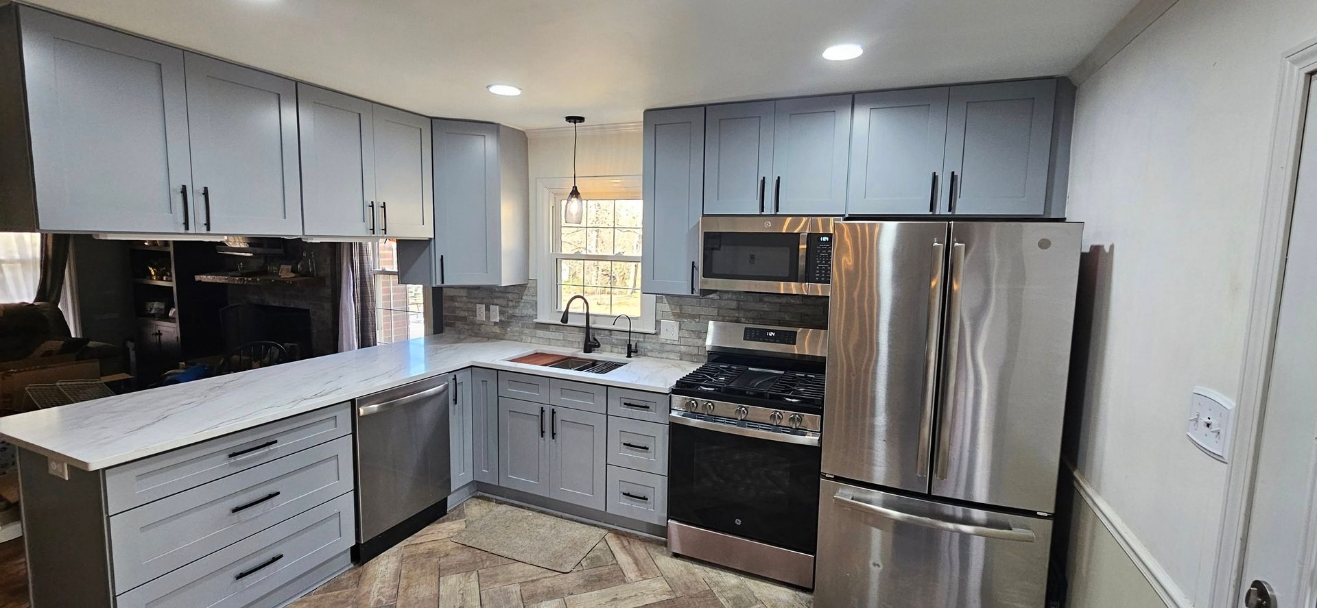 A modern kitchen with light gray cabinets, stainless steel appliances, white countertops, and wood-patterned flooring.