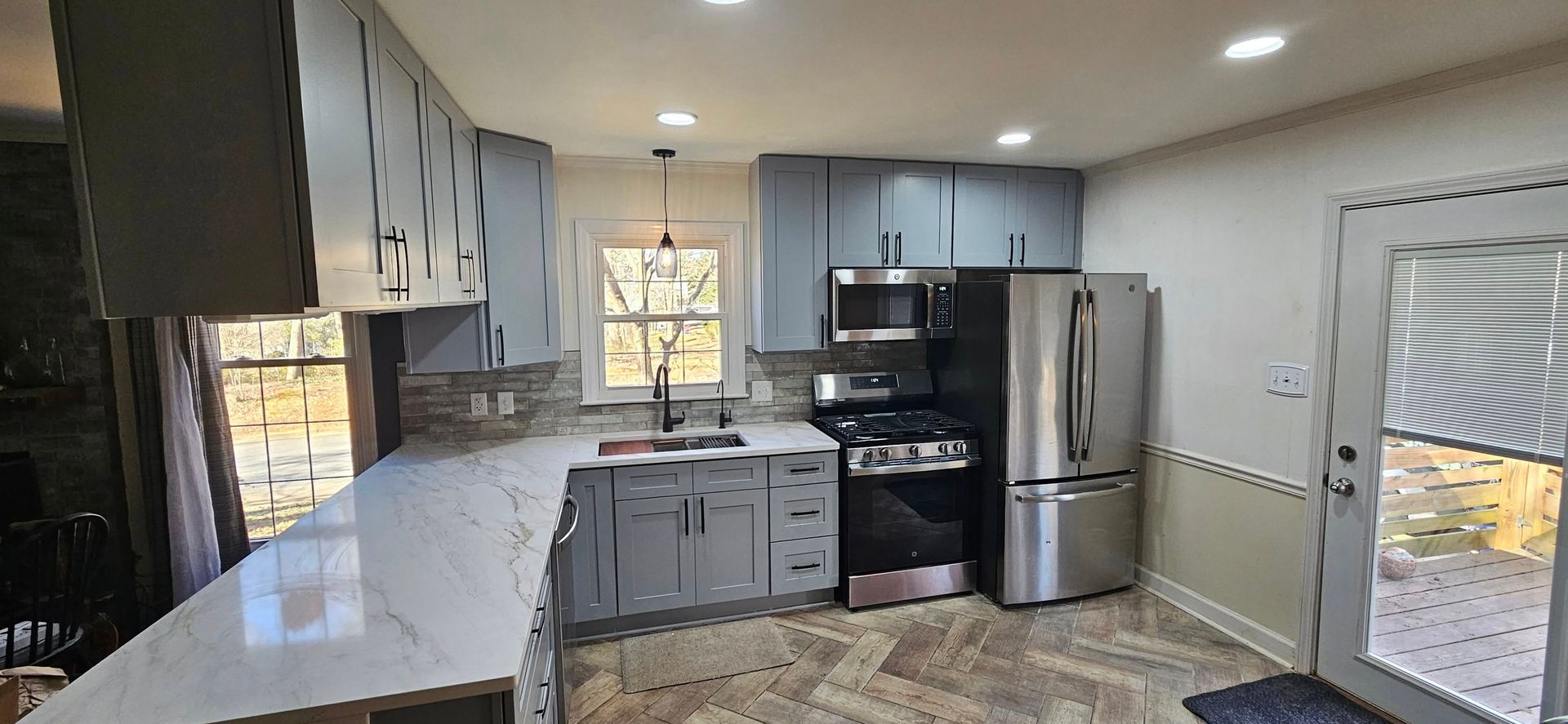 A modern kitchen featuring grey cabinets, a marble-patterned countertop, stainless steel appliances, and tiled flooring.
