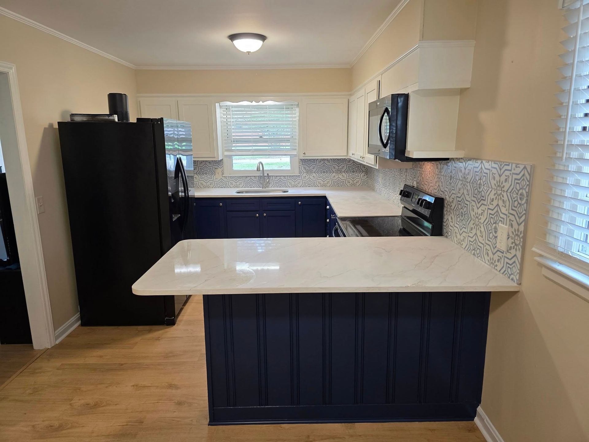 A kitchen with a dark blue island and lower cabinets, white countertops, a black refrigerator, and a tiled backsplash.