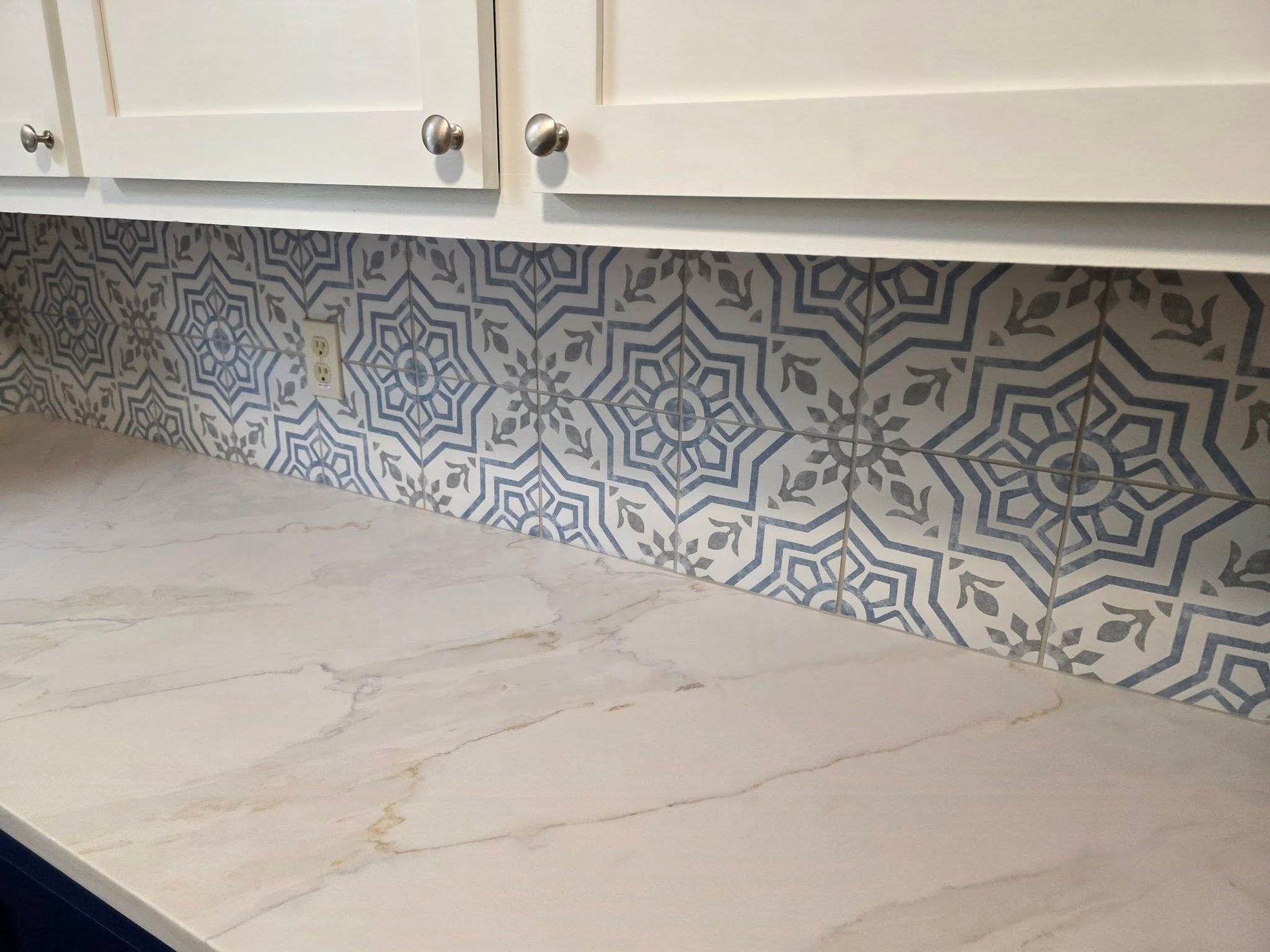 White kitchen cabinets above a light, marble-patterned countertop with a decorative blue and white patterned backsplash.