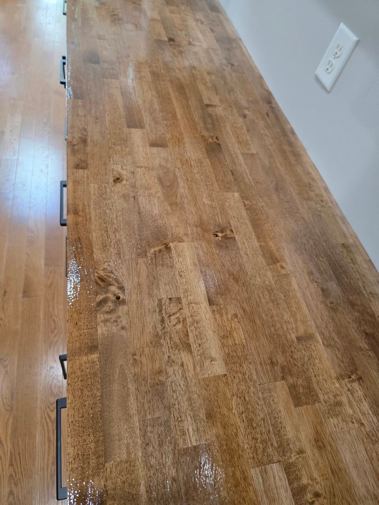 A high-angle view of a wood butcher block countertop with a glossy finish, positioned next to a white wall with an outlet.